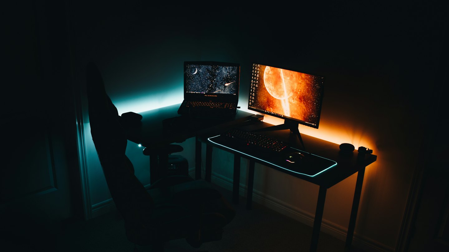 Mesa de jogo com notebook, monitor e iluminação colorida.