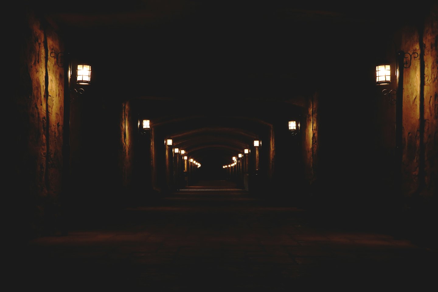 Túnel de pedra antigo iluminado por arandelas.