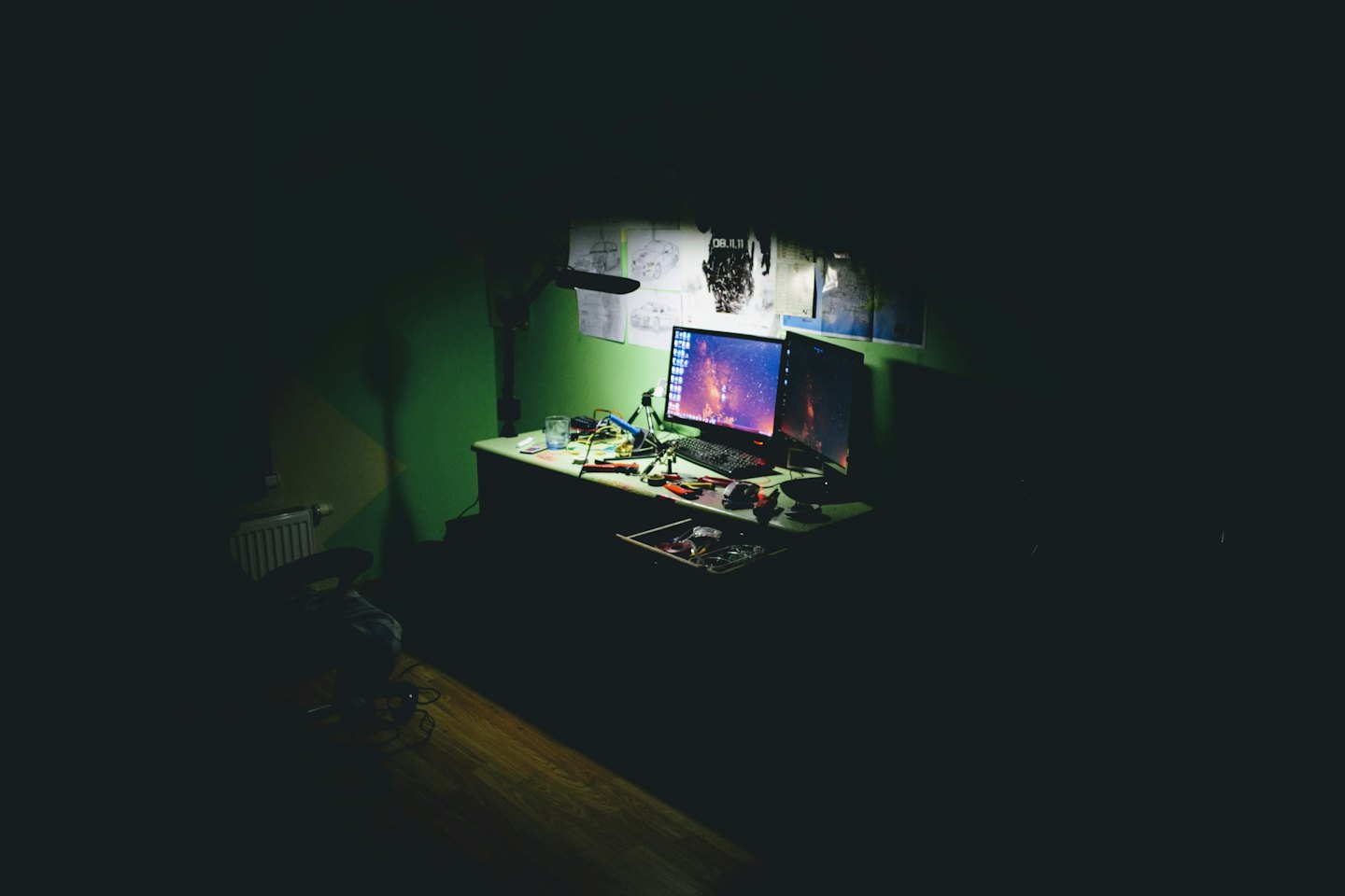Mesa de trabalho com computadores e ferramentas sob a luz de uma luminária.